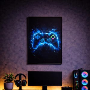 May include: A gaming setup with a framed poster of a glowing blue game controller. The desk includes a monitor, keyboard, mouse, headphones, and a computer tower with colourful LED lights. A small plant adds a touch of green.