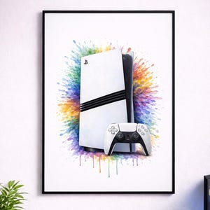 May include: Framed print of a white games console and controller, with a vibrant watercolour splash background. The console has black detailing. The image is on a desk with gaming accessories, including a keyboard, mouse, and headphones.