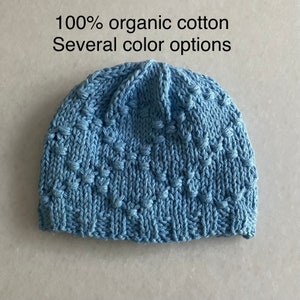 May include: A blue knitted beanie hat made from 100% organic cotton. The hat has a textured pattern and is available in several colors.