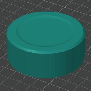 May include: A teal-colored, cylindrical object with a flat top and a slightly recessed center. The object has a smooth, solid appearance and is set against a dark gray grid background. The design is simple and geometric.