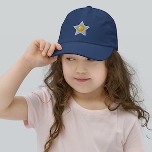 Könnte beinhalten: Eine marineblaue Baseballkappe mit einem weißen Stern und einem gelben Kreis in der Mitte. Der Stern ist auf der Vorderseite der Kappe gestickt.