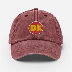 May include: A maroon vintage-style baseball cap with a red circle and the letters "DK" in yellow.