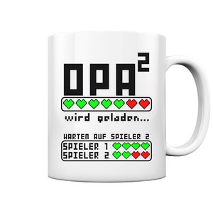 Könnte beinhalten: Weiße Keramiktasse mit einem schwarzen und grünen Pixel-Design, auf dem "OPA²" und "wird geladen..." mit einer Fortschrittsanzeige aus grünen Herzen und einem roten Herzen steht. Unter der Fortschrittsanzeige steht der Text "WARTEN AUF SPIELER 2" und zwei weitere Fortschrittsanzeigen mit dem Text "SPIELER 1" und "SPIELER 2" mit grünen Herzen und einem roten Herzen.