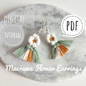 May include: A pair of macrame flower earrings with green, white, and orange tassels. The earrings are on a gray marble surface. The text "DIGITAL TUTORIAL" and "PDF" are in the image.