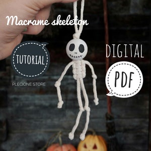 May include: A cream-coloured macrame skeleton with a painted wooden head, suspended by a loop. The image includes the words "Macrame skeleton", "Tutorial", and "Digital PDF". Two carved pumpkins are also visible in the image.