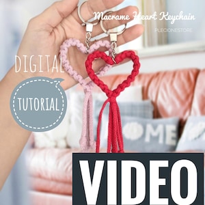 以下が含まれることがあります： 銀色のキーリングが付いた、ピンクと赤の2つのマクラメハートキーホルダー。キーホルダーは手にぶら下がっていて、その下に「デジタルチュートリアルビデオ」というテキストが表示されています。