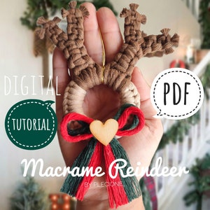 May include: A brown macrame reindeer ornament with a red and green bow and a wooden heart. The ornament is held in a hand. The text "DIGITAL TUTORIAL PDF" is in the image.