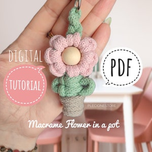 Puede incluir: Un tutorial digital en PDF para hacer un llavero de macramé con una flor en una maceta. La flor es rosa con un centro de cuentas de madera y hojas verdes. La maceta es beige. El texto "TUTORIAL DIGITAL" y "PDF" está en bocadillos de diálogo.