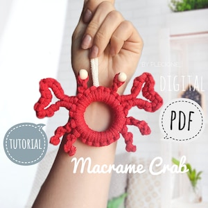 Könnte beinhalten: Ein roter Makramee-Krabbe mit weißen Perlen als Augen. Der Krabbe hängt an einer weißen Schnur. Das Bild enthält den Text "DIGITAL PDF" und "Macrame Crab".
