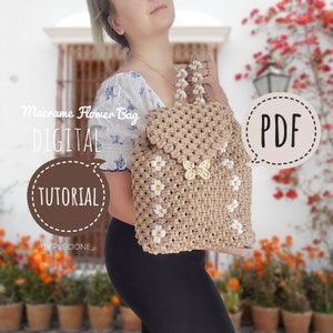 Op de afbeelding: Een beige macramé bloemen tas met witte margriet accenten en een gouden vlinder bedel. De tas is een rugzak stijl met een trekkoord sluiting. De afbeelding bevat de tekst "Macrame Flower Bag DIGITAL TUTORIAL BY PLECIONE_ PDF".
