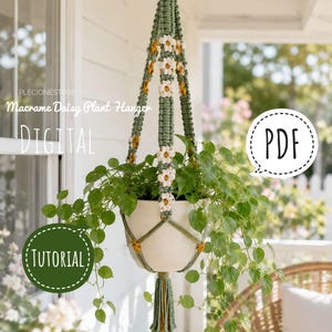 Puede incluir: Un colgador de plantas de macramé en color verde salvia con detalles de margaritas blancas y amarillas, un anillo de madera en la parte superior y una borla en la base. Sostiene una maceta blanca con una planta verde. El texto dice Macrame Daisy Plant Hanger.