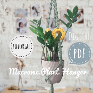 Pode incluir: Um suporte de planta de macramé verde com anéis de macramé amarelos, segurando uma planta em vaso. O suporte está pendurado em uma parede de tijolo branco. O texto "DIGITAL PDF" e "TUTORIAL" estão em balões de fala. O texto "BY PLECIONE" e "Macrame Plant Hanger" estão abaixo do suporte.