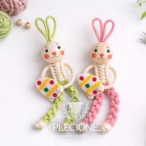 May include: Two handmade macrame bunny figures with wooden heads, holding Easter egg-shaped ornaments. One bunny has green ears and legs, the other pink. The eggs are white with colourful dots. The brand name "PLECIONE HANDMADE" is visible.