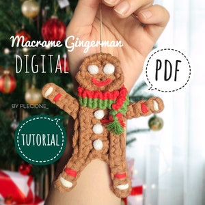 Könnte beinhalten: Ein brauner Makramee-Lebkuchenmann-Anhänger mit weißen Knöpfen, rotem und grünem Schal und einer weißen Schnur zum Aufhängen. Der Anhänger wird in einer Hand vor einem verschwommenen Hintergrund eines Weihnachtsbaums und Geschenken gehalten. Der Text "Macrame Gingerman DIGITAL PDF TUTORIAL" ist auf dem Bild zu sehen.