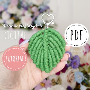 Può includere: Un portachiavi a forma di foglia verde in macramè con un fermaglio a forma di cuore argentato. Il portachiavi è tenuto in una mano con uno sfondo floreale. Il testo "Macrame Leaf Keychain DIGITAL TUTORIAL PDF" è visibile nell'immagine.