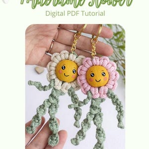 Op de afbeelding: Twee handgemaakte macram&eacute; bloem sleutelhangers. E&eacute;n heeft een cr&egrave;mekleurige bloem, de andere is roze. Beide hebben gele gezichten met lachende uitdrukkingen en groene stelen en benen. De tekst "Macrame Flower Digital PDF Tutorial" staat bovenaan.