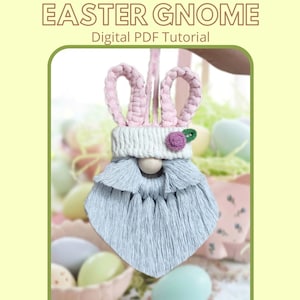May include: A macrame Easter gnome with pink bunny ears, a white hat with a pink flower, and a light blue beard. The gnome is hanging from a string and is surrounded by Easter eggs.