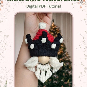 May include: A macrame nutcracker ornament with a red and black crown, white beard, and wooden face. The ornament is held in a hand against a blurred background of a Christmas tree. The text "Macrame Nutcracker" and "Digital PDF Tutorial" is displayed above the ornament.