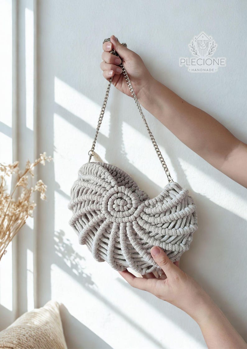 May include: A light grey macrame handbag with a silver chain strap. The bag features a distinctive spiral design on the front. The bag is handmade and held by a person's hands. The brand name "Plecione Handmade" is visible on the upper right.