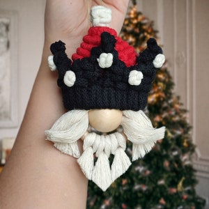 May include: A handmade Christmas ornament featuring a gnome with a red and black crown, white beard, and wooden bead nose.