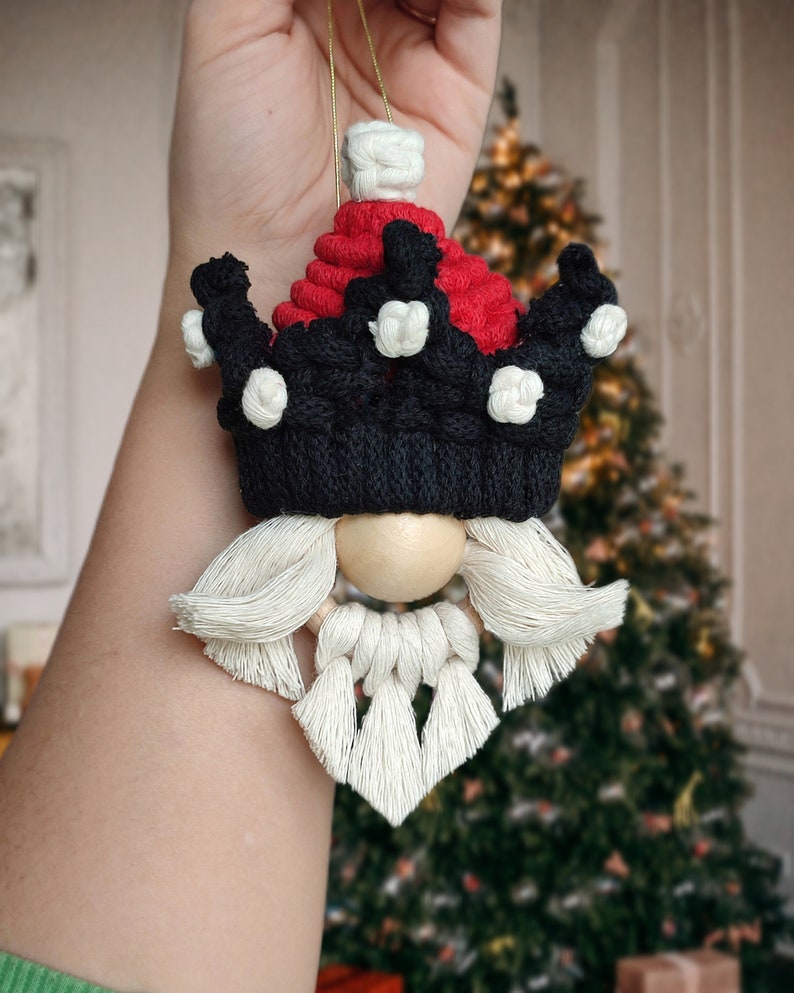 May include: A handmade Christmas ornament featuring a gnome with a red and black crown, white beard, and wooden bead nose.