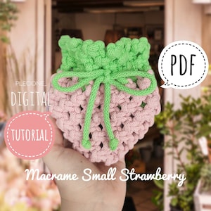 May include: A pink and green macrame strawberry-shaped pouch with a drawstring closure. The pouch is held in a hand and the text "PDF" is in a speech bubble above the pouch. The text "DIGITAL TUTORIAL" is in a pink circle on the left side of the image. The text "Macrame Small Strawberry" is below the pouch.