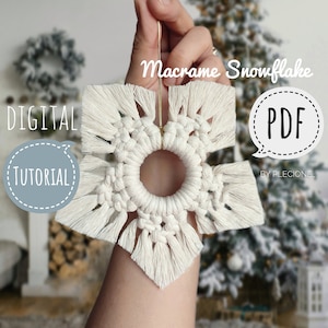 Puede incluir: Un adorno de copo de nieve de macramé blanco con un cordón dorado. El adorno se sostiene en una mano sobre un fondo borroso de un árbol de Navidad. El texto "Macrame Snowflake" y "PDF" es visible en la imagen.