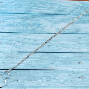 Puede incluir: Un collar plateado con un colgante de la cabeza de Mickey Mouse. El colgante es un contorno simple de la cara del personaje. La cadena tiene un dise&ntilde;o tejido. El collar se exhibe sobre una superficie de madera azul claro.