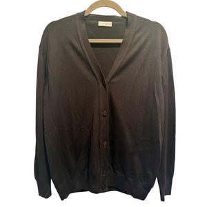 May include: A dark brown cardigan sweater with a V-neck and button closure. The long-sleeved sweater is hanging on a wooden hanger against a white background. The sweater has a simple, classic design.