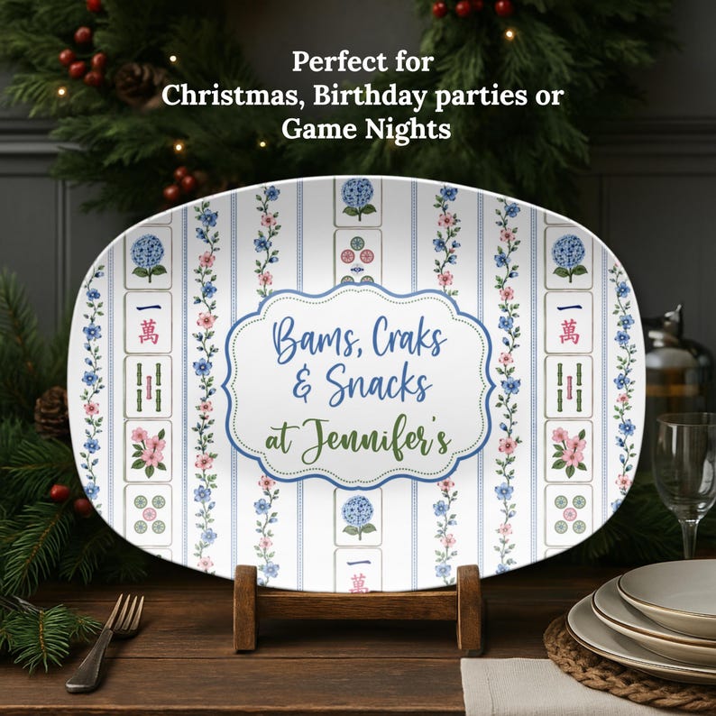 Puede incluir: Una bandeja de servir ovalada con fondo blanco, rayas azules verticales y enredaderas florales. La bandeja muestra ilustraciones de fichas de Mahjong y una etiqueta central con borde azul con el texto Bams, Craks & Snacks at Jennifer's.