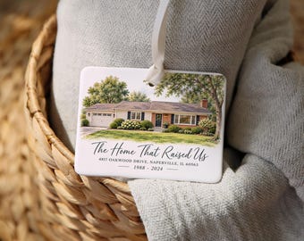 May include: A rectangular white ceramic ornament featuring a watercolor illustration of a single-story house with a garage and lawn. The text reads: The Home That Raised Us, 4817 Oakwood Drive, Naperville, IL 60563, and the years 1988 - 2024.