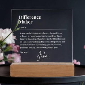 May include: A clear acrylic plaque with the text "Difference Maker" defined as "A very special person who changes lives daily. An ordinary person who accomplishes extraordinary things by inspiring others to be the best that they can be. Someone who makes the impossible possible and the difficult easier by modeling passion, wisdom, goodness, and joy. One of life's greatest gifts." The plaque also includes the text "See also: Julia" in cursive.