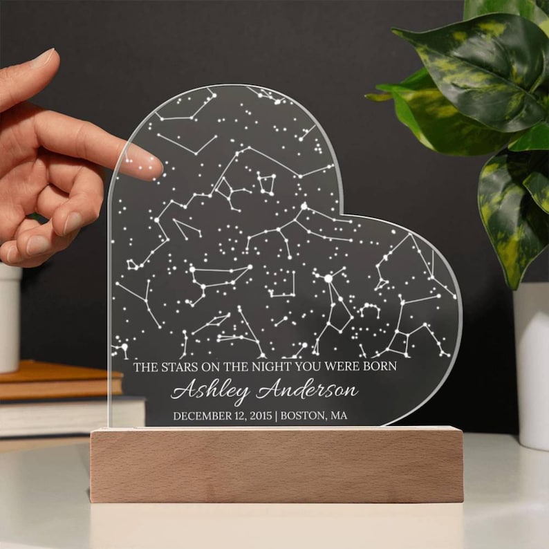May include: A heart-shaped night light featuring a constellation map with the text "THE STARS ON THE NIGHT YOU WERE BORN", the name "Ashley Anderson", and the date "DECEMBER 12, 2015 | BOSTON, MA". The base is made of wood.