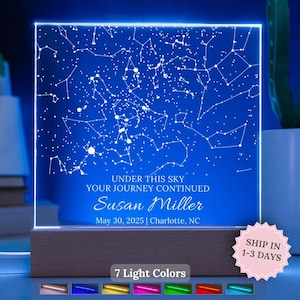 Puede incluir: Una luz de noche personalizada con un fondo azul, que presenta un mapa de constelaciones y el texto "UNDER THIS SKY YOUR JOURNEY CONTINUED" con un nombre, fecha y ubicación. La base es de madera y ofrece 7 colores de luz.