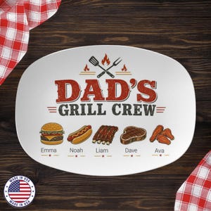 Peut inclure: Plat ovale blanc avec le texte "DAD'S GRILL CREW" en rouge et noir. L'assiette présente des illustrations d'un hamburger, d'un hot-dog, de côtes levées, d'un steak et d'ailes de poulet, avec des noms en dessous.