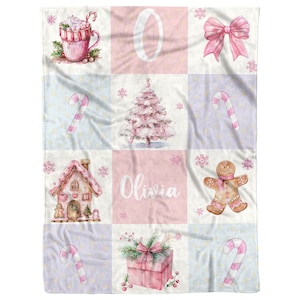 May include: A pink and blue Christmas themed baby blanket with a gingerbread house, a Christmas tree, a candy cane, a gingerbread man, a gift box, a hot chocolate mug, a bow, and the name Olivia.