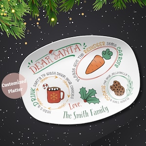 May include: White oval ceramic serving platter with a Christmas theme. It features a red mug with hot chocolate and marshmallows, a carrot, two chocolate chip cookies, and the text "Dear Santa! Please give the reindeer some carrots. Here's a cookie for your jolly belly. Please take a cookie for your jolly belly. Love, The Smith Family."