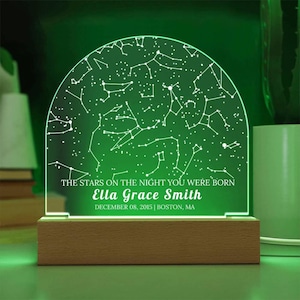 May include: A personalized night light with a constellation design. The green-lit acrylic panel displays a star map and the text "THE STARS ON THE NIGHT YOU WERE BORN" with a name and date. It sits on a wooden base.