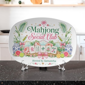 Peut inclure: Un plateau de service ovale blanc portant le texte Mahjong Social Club et Hosted by Samantha. Le motif comprend des illustrations de tuiles de mah-jong, de verres à martini avec olives, de fleurs roses, de vases bleus et blancs et d'agrumes.