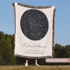May include: A cream-colored woven throw blanket with a black and white star map design in a circular frame. The blanket has a fringed edge and features the names "Katie & Aaron" and the text "THE START OF OUR 'US' June 23, 2019 | Barcelona, Spain."