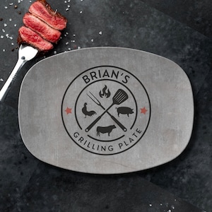 May include: A gray oval-shaped grilling plate with a black and white logo that says "BRIAN'S GRILLING PLATE". The logo features a rooster, pig, cow, and a spatula and fork crossed over each other with a flame above them.