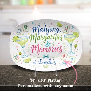 May include: An oval platter with the words "Mahjong, Margaritas & Memories" in colorful script. The design includes margarita glasses, lime slices, and Mahjong tiles. The platter measures 14 inches by 10 inches.