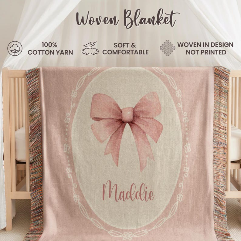May include: A pink woven blanket with a watercolour bow design and the name "Maddie" in script. The blanket is draped over a cot and features the text "Woven Blanket", "100% Cotton Yarn", and "Soft & Comfortable".