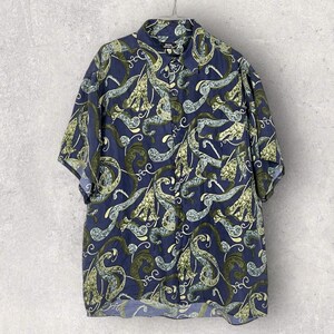 Può includere: Una camicia blu a maniche corte con bottoni e un motivo paisley verde e bianco.