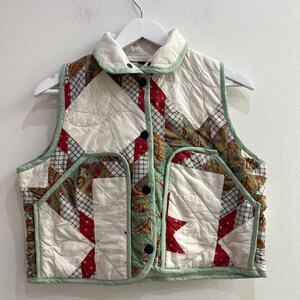 Può includere: Un gilet trapuntato senza maniche con un design patchwork in tessuto a motivi color crema, rosso, blu e verde. Il gilet presenta un colletto, una chiusura frontale con bottoni scuri e due tasche anteriori, il tutto rifinito con un bordo verde chiaro.