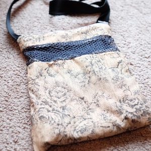 May include: A small beige fabric bag with a black strap and a black mesh panel. The bag has a floral pattern.
