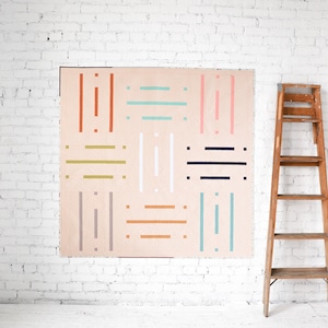 Könnte beinhalten: Ein rosafarbener Quilt mit einem geometrischen Muster aus bunten Linien. Der Quilt hängt an einer weißen Backsteinwand neben einer Holzleiter.