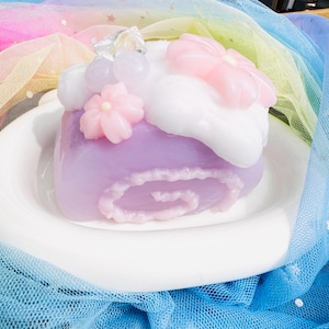 Peut inclure: Un gâteau en spirale violet et blanc avec des fleurs roses et un nuage blanc sur le dessus. Le gâteau est sur une assiette blanche et un tissu tulle bleu et blanc.