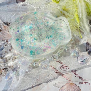 May include: A clear resin fish-shaped dish with iridescent glitter embedded inside. The dish is filled with a variety of colors, including pink, blue, and green.