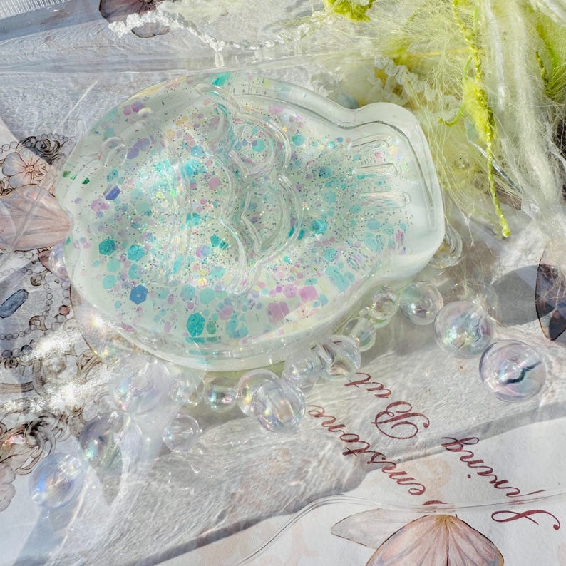 May include: A clear resin fish-shaped dish with iridescent glitter embedded inside. The dish is filled with a variety of colors, including pink, blue, and green.